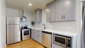 A modern kitchen with stainless steel appliances, white cabinetry, and a wooden floor.