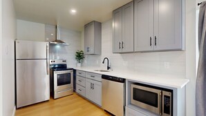 Een moderne keuken met roestvrijstalen apparatuur, witte kastjes en een houten vloer.