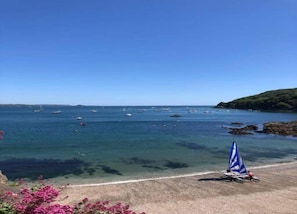 Une vue sur la côte, avec une eau claire, des bateaux et une plage de sable bordée d’un parasol bleu.