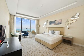A hotel room with a large bed, a desk, a chair, and a view of the sea.