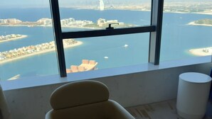 A high-rise room with a large window overlooking a coastal cityscape, including a prominent sailboat and a city skyline. - Gorgeous luxury studio - Exquisite Palm View (Palm Jumeirah)