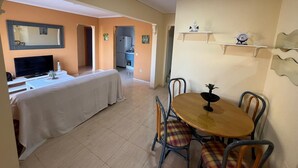 A room with a dining table, chairs, a TV, and a kitchen area. - Bungalow with pool, private patio of 17m2 and terrace (Playa del Carabassi) (Gran Alacant)