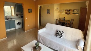 A living room with a white sofa, a white coffee table, and a kitchen area in the background. - Bungalow with pool, private patio of 17m2 and terrace (Playa del Carabassi) (Gran Alacant)