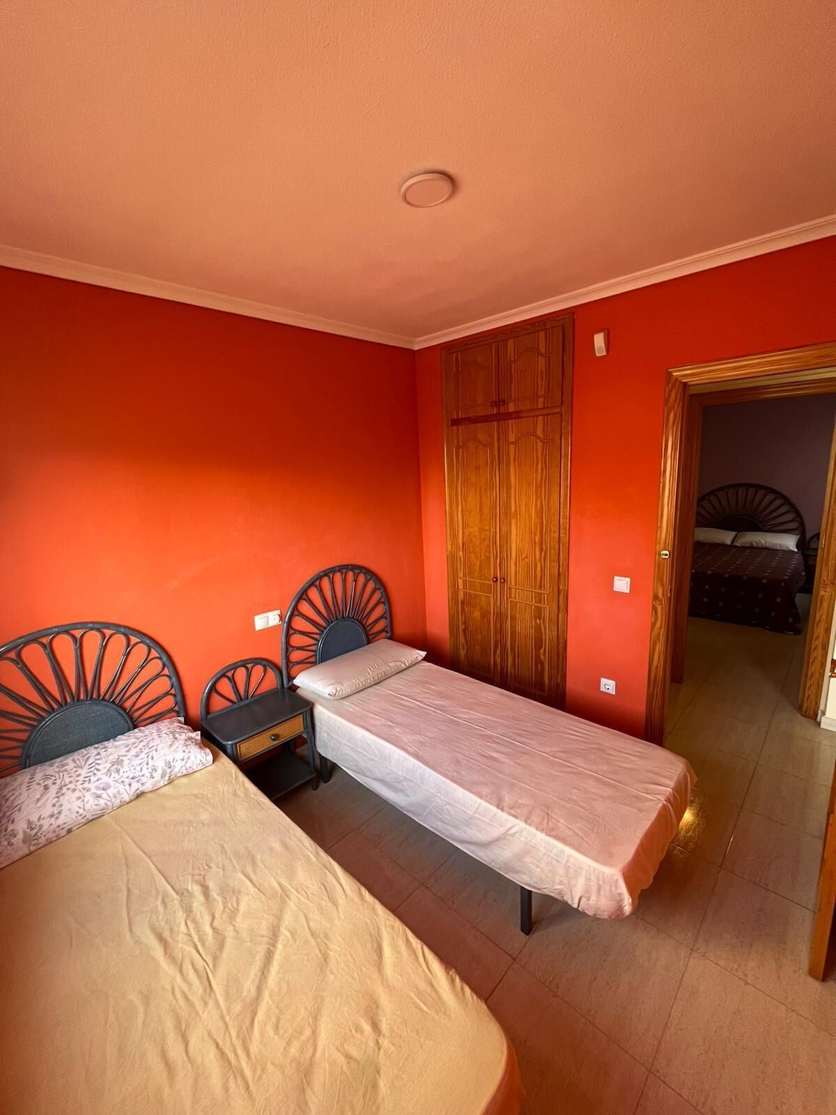 A room with two single beds, a wooden wardrobe, and a door leading to another room.