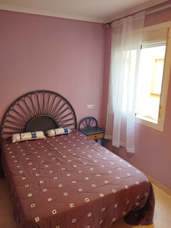 A bedroom with a bed, a small table, and a window with curtains.