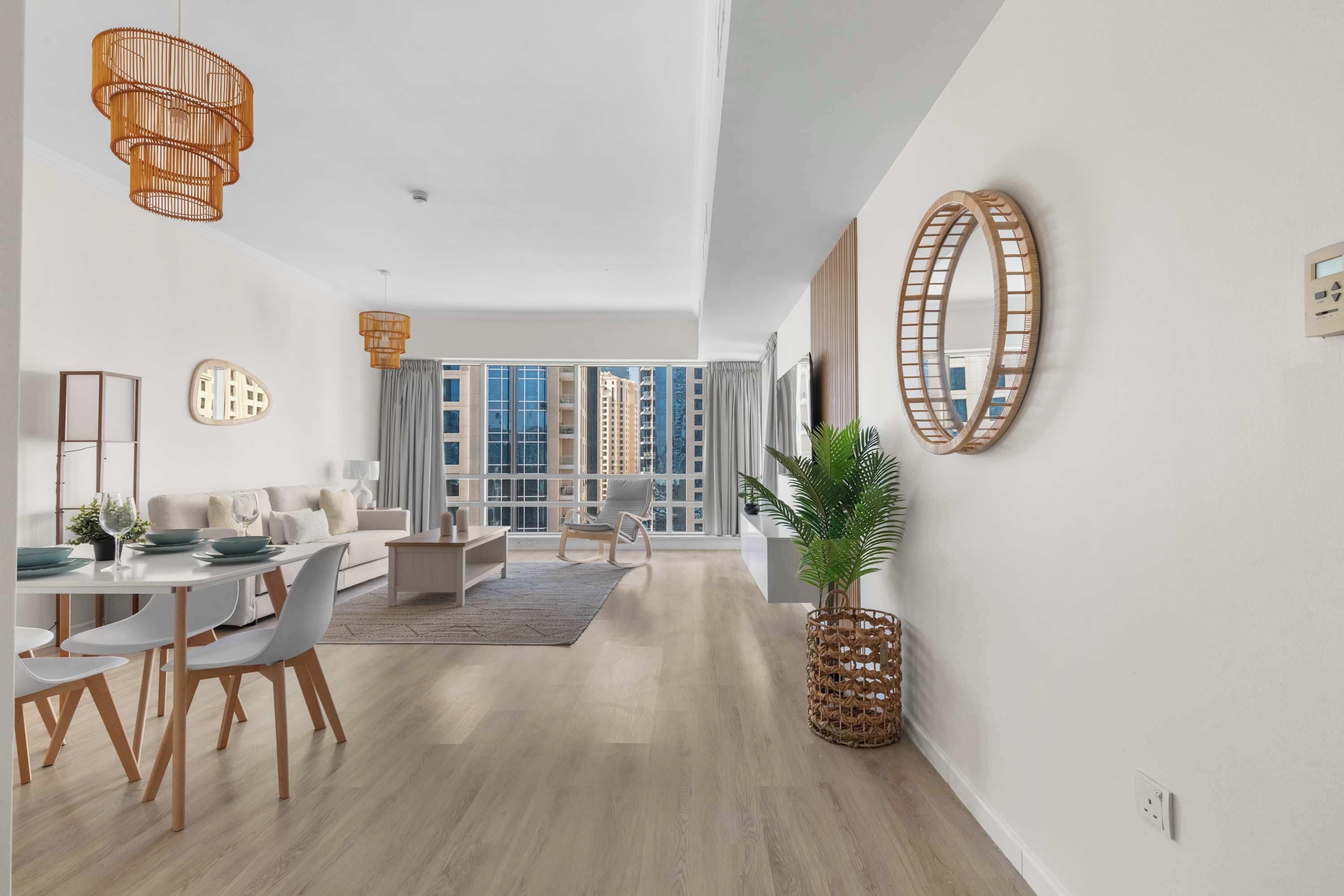 A spacious living area with a dining table, sofa, and chairs, large windows, and modern decor.