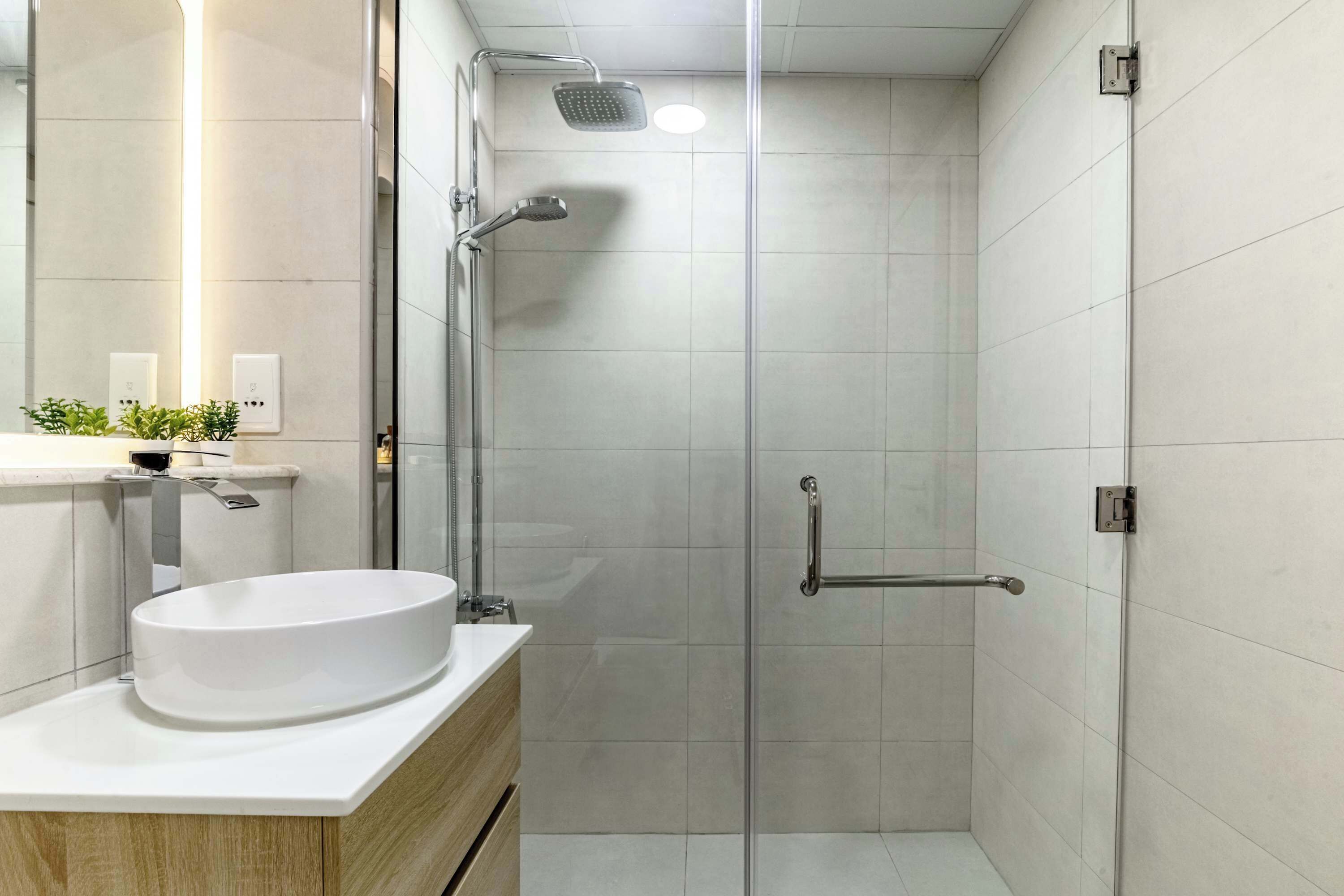 A modern bathroom with a glass shower enclosure, a white sink, and a mirror.