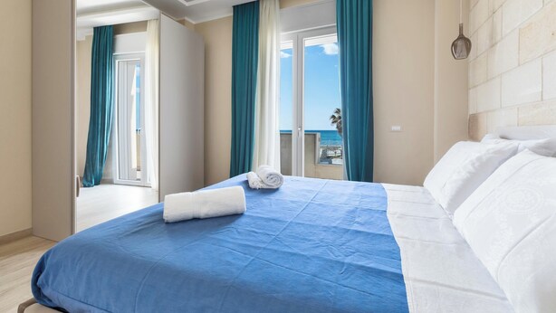 A hotel room with a large bed, a balcony with a view, and a door leading to another room.