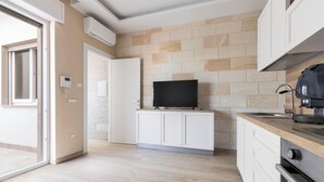 A modern kitchen with a flat-screen TV, white cabinets, and a wooden countertop.