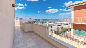 A balcony with a view of the sea and a parking area.