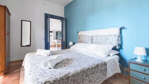 A neatly made bed with a patterned bedspread, a bedside table with a lamp, and a wooden wardrobe.