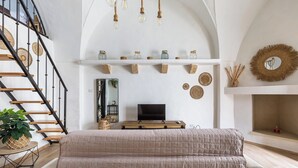 A bedroom with a large bed, a TV on a wooden stand, a staircase, and decorative wall items.