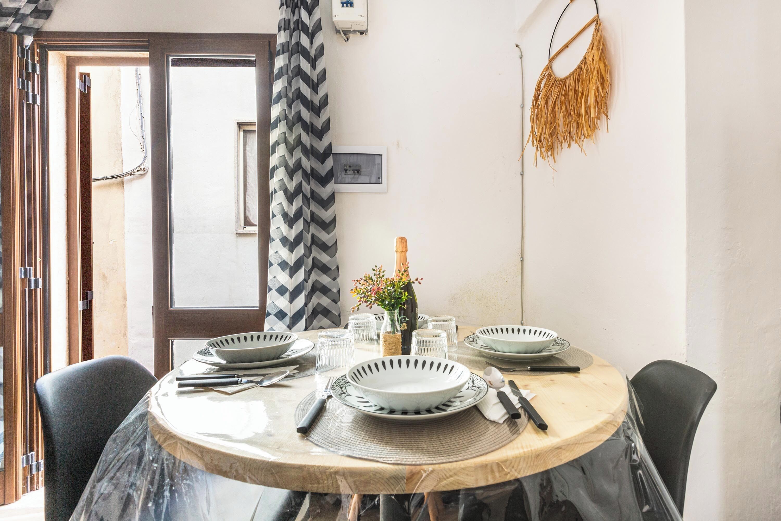 Una mesa de comedor dispuesta con platos, vasos, cubiertos, un florero con flores y una botella de champán.