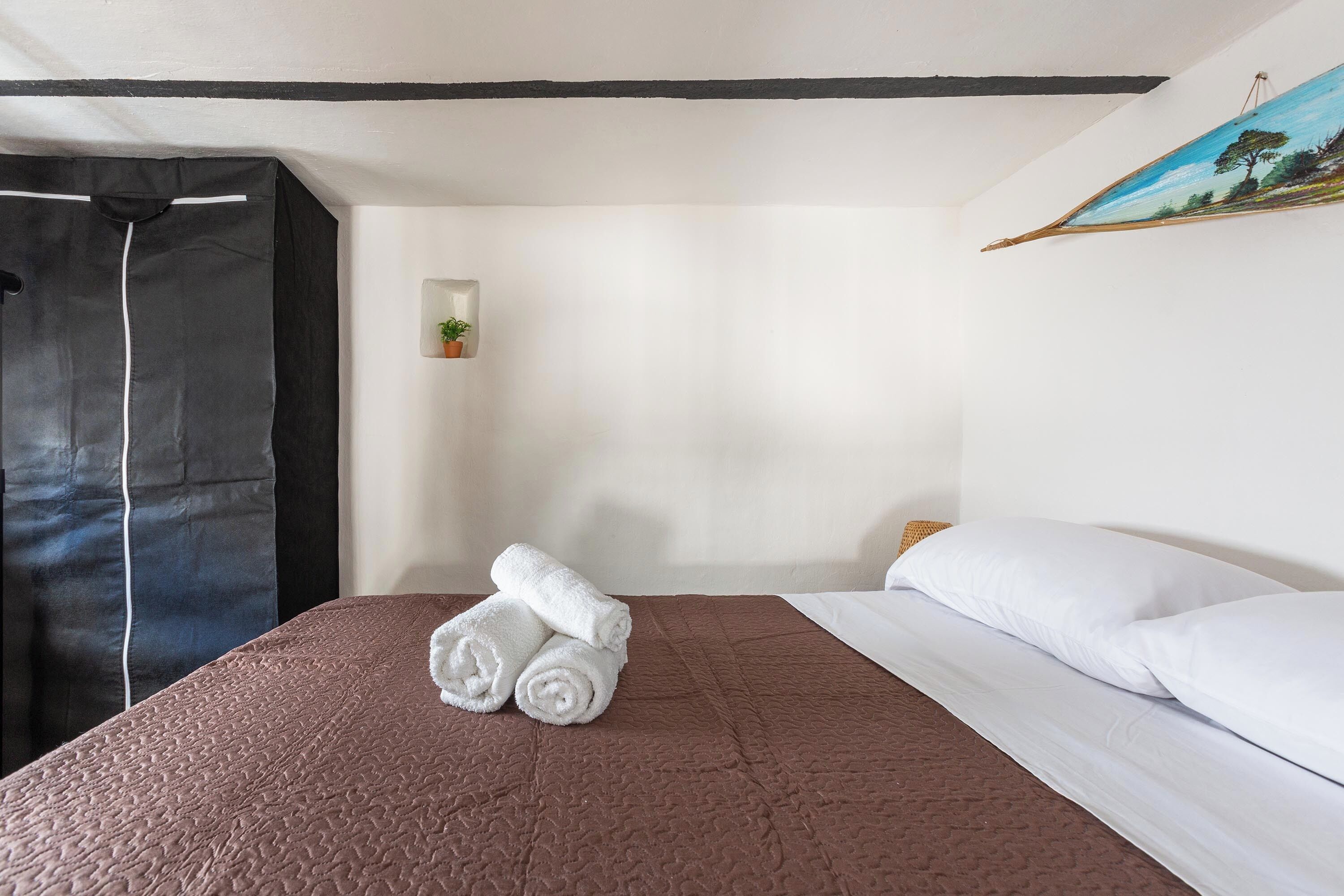 A hotel room with a brown textured bedspread, white pillows, and a neatly folded white towel on the bed.