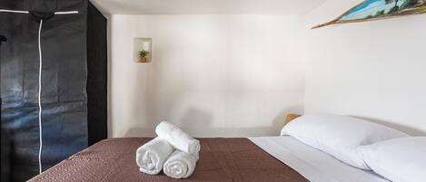A hotel room with a brown textured bedspread, white pillows, and a neatly folded white towel on the bed.
