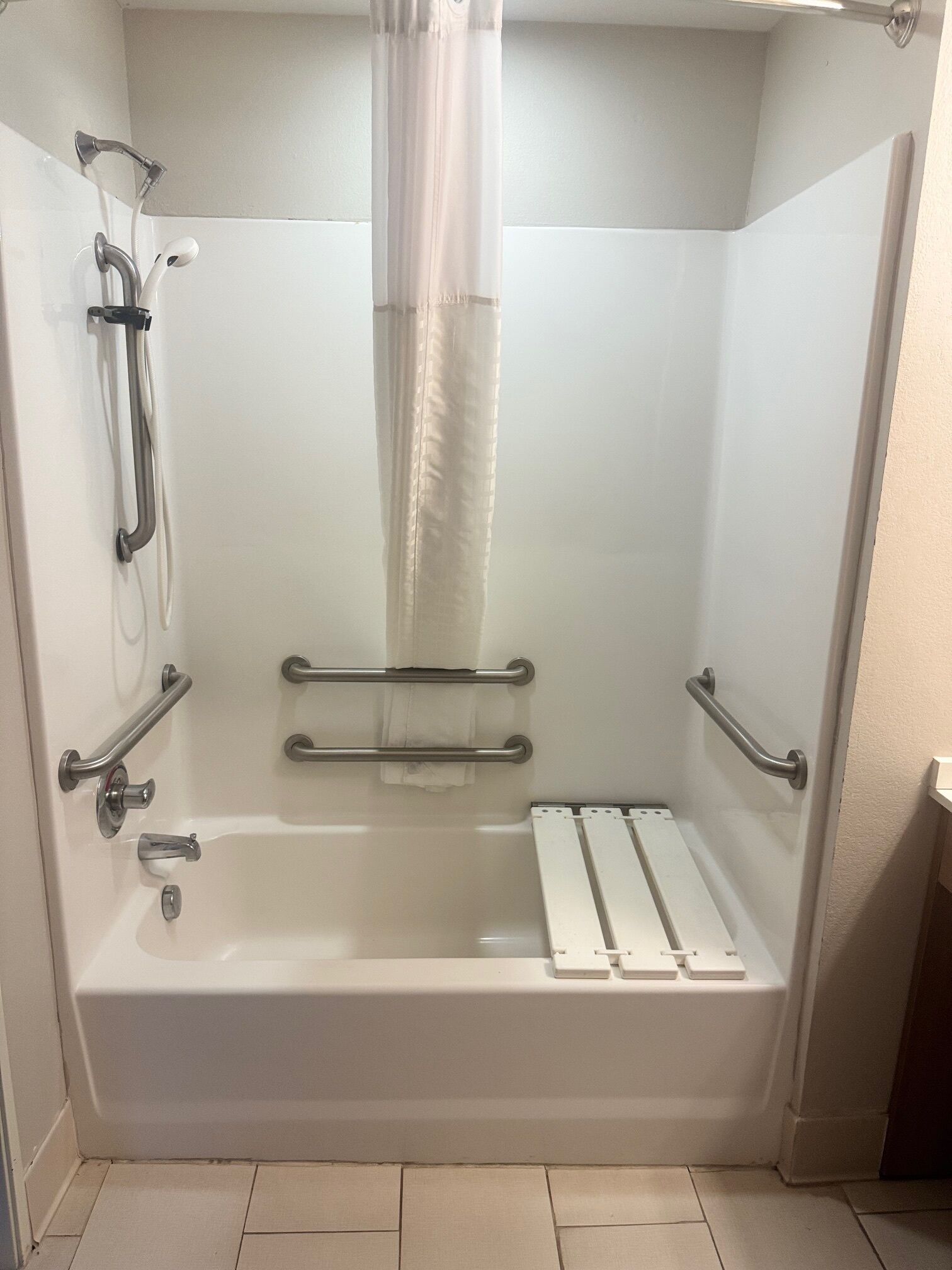 A standard white bathroom with a bathtub, grab bars, and a showerhead.
