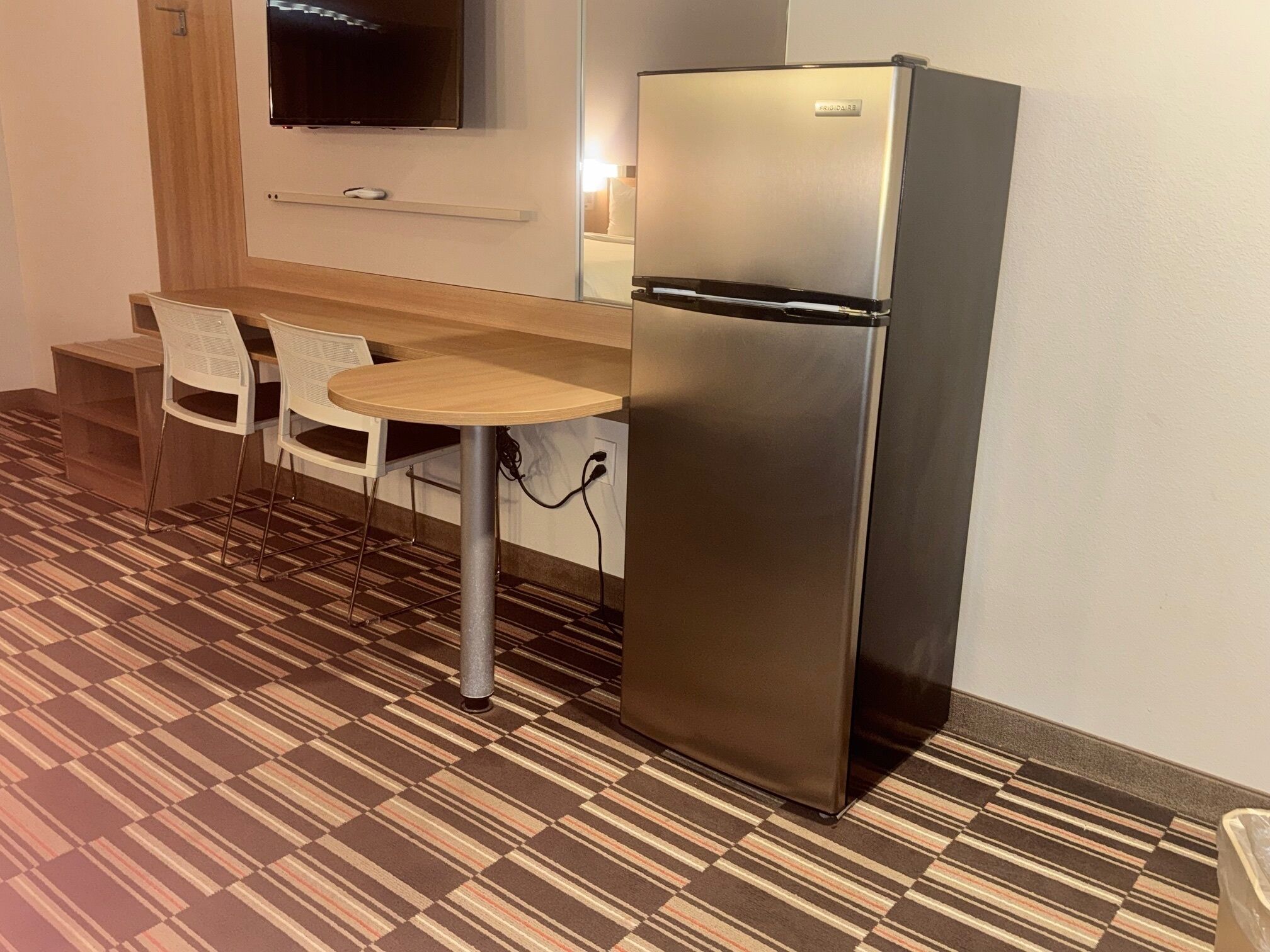 A compact kitchenette with a refrigerator, a small table, two chairs, and a patterned floor.