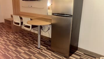 Una kitchenette compacta con refrigerador, una mesita, dos sillas y piso estampado.