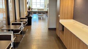 A clean, modern cafeteria with stainless steel tables and chairs, a long counter, and a bright, well-lit interior. - Permian Studio Apartments (Monahans)
