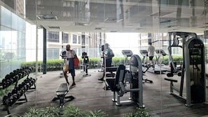 Un gimnasio con equipo de ejercicio, incluyendo cintas de correr y máquinas de pesas, y un muro de vidrio que ofrece vistas a la ciudad.