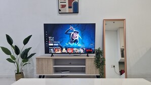 Una sala de estar moderna con un televisor de pantalla plana montado en la pared, un mueble de madera debajo, una mesa de centro blanca en primer plano y una planta en maceta a la izquierda.