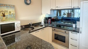 A modern kitchen with white cabinets, a stainless steel oven, a microwave, and a granite countertop. - Apartment Near Belgian Coast With Terrace (Knokke-Heist)