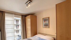 A hotel room with a bed, a window with curtains, a wooden wardrobe, and a poster on the wall. - Apartment Near Belgian Coast With Terrace (Knokke-Heist)