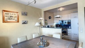 A dining area with a large table, chairs, a coffee machine, and a kitchen in the background. - Apartment Near Belgian Coast With Terrace (Knokke-Heist)
