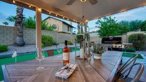 An outdoor patio with a wooden table, wine glasses, a bottle of wine, and a grill. - Private Pool & Putting Green | Fire Pit Patio (Scottsdale)