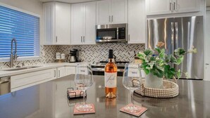 A modern kitchen with white cabinets, stainless steel appliances, and a central island with wine glasses and a bottle. - Private Pool & Putting Green | Fire Pit Patio (Scottsdale)