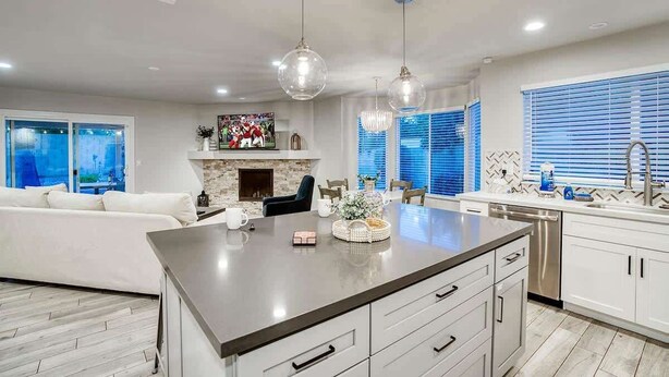 A modern kitchen with a central island, pendant lights, a fireplace, and a dining area with a sofa and chairs. - Private Pool & Putting Green | Fire Pit Patio (Scottsdale)