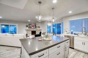 A modern kitchen with a central island, pendant lights, a fireplace, and a dining area with a sofa and chairs. - Private Pool & Putting Green | Fire Pit Patio (Scottsdale)