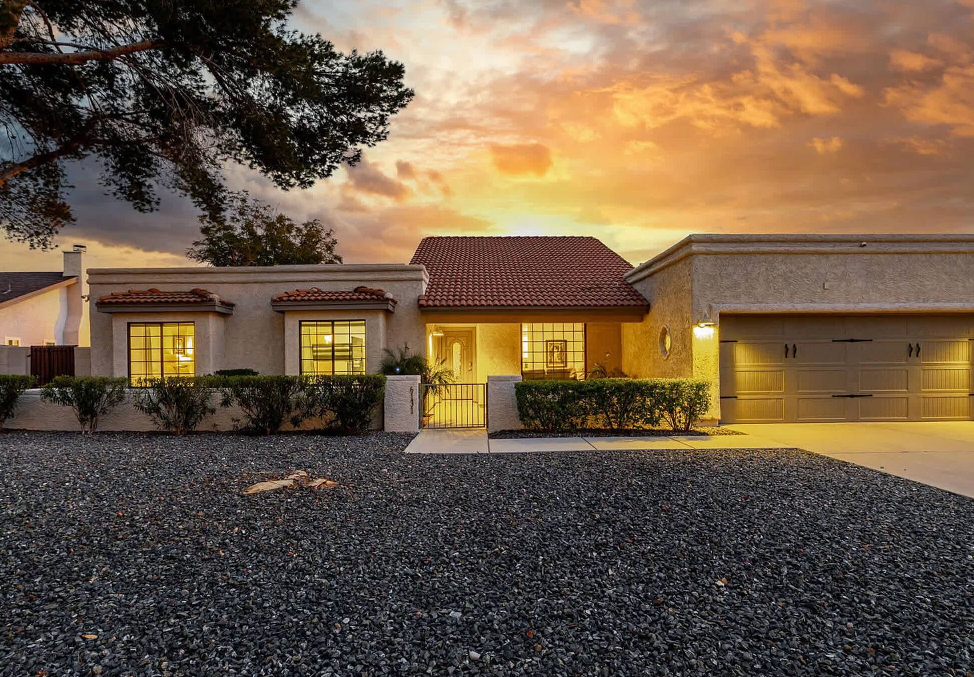 A two-story house with a red-tiled roof, a garage, and a gravel driveway.