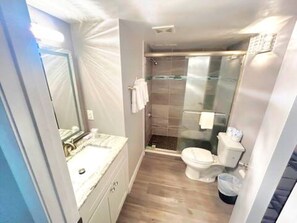 Un baño con suelo de madera, un lavabo blanco, un inodoro y una cabina de ducha de cristal.