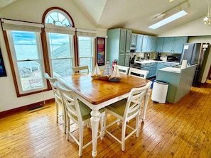 A kitchen with wooden cabinets, a dining table with chairs, and a view through the windows. - Waterfront Beach Home-3Bdrms/2Bth-close to everything! (Huron)