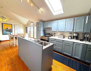 A modern kitchen with grey cabinets, a central island with a sink, and a dining area with a table and chairs. - Waterfront Beach Home-3Bdrms/2Bth-close to everything! (Huron)