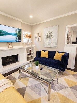 A living room with a fireplace, a sofa, a coffee table, and a television. - Modernized Cherry St. Historic Gem – Quiet Cul-De-Sac Home (Tulsa)