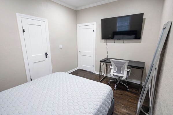 A bedroom with a bed, a desk with a chair, a television mounted on the wall, and two doors. - Modernized Cherry St. Historic Gem – Quiet Cul-De-Sac Home (Tulsa)