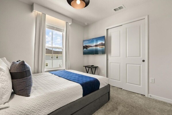 A bedroom with a bed, a window, a wall-mounted TV, and a door.