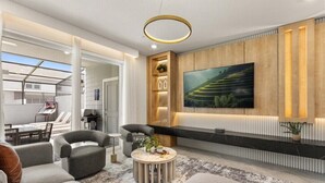 A modern living room with a large TV, comfortable seating, and a wooden accent wall. - 5 BD/ 4.5 BA/ Windsor Cay (16053 BW) (Clermont)