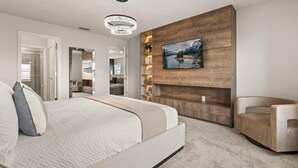 A modern bedroom with a large bed, a mounted TV, a wooden accent wall, and a chandelier. - 5 BD/ 4.5 BA/ Windsor Cay (16053 BW) (Clermont)