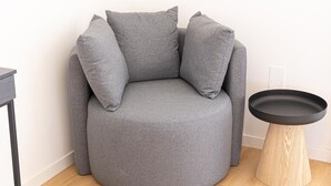 A grey, round, upholstered chair with multiple cushions, positioned next to a small wooden side table with a black tray. - Apartment in Via di Santa Costanza, a short distance from Corso Trieste (Rome)