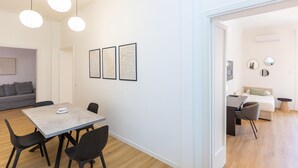 A modern living room with a grey sofa, a dining table with chairs, and a kitchen area visible through an open door. - Apartment in Via di Santa Costanza, a short distance from Corso Trieste (Rome)