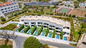 A modern hotel with multiple swimming pools, a tennis court, and solar panels.