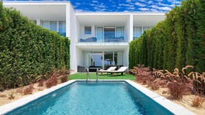 A modern pool area with a clear blue pool, lounge chairs, and a two-story building with large windows and a balcony.
