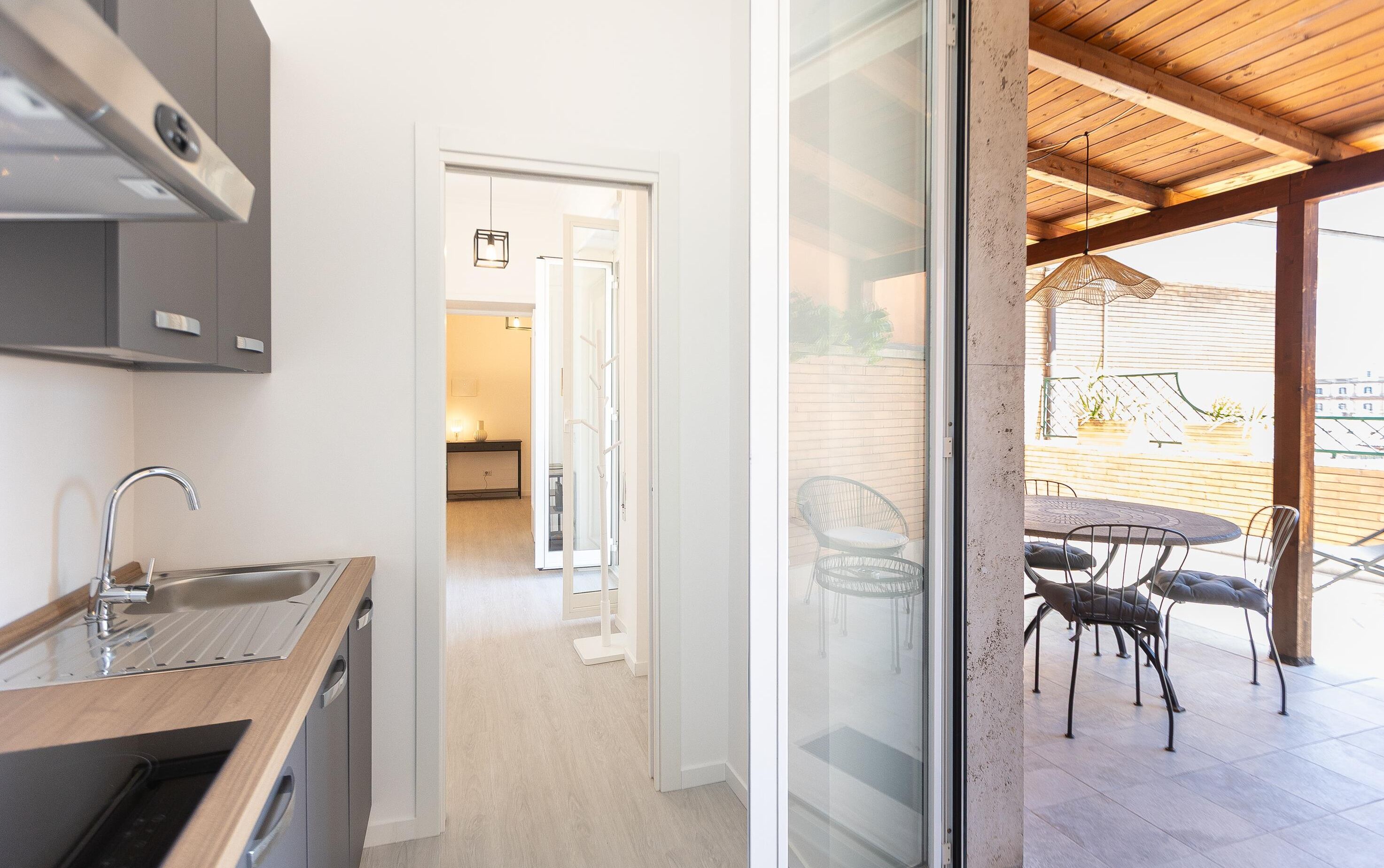 Eine moderne Küche mit eingebautem Spülbecken und Schränken, eine Glastür führt zu einem Balkon mit Sitzgelegenheit.