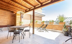A covered patio with a round table and chairs, potted plants, and a view of the cityscape. - Constance Terrace apartment (Rome)