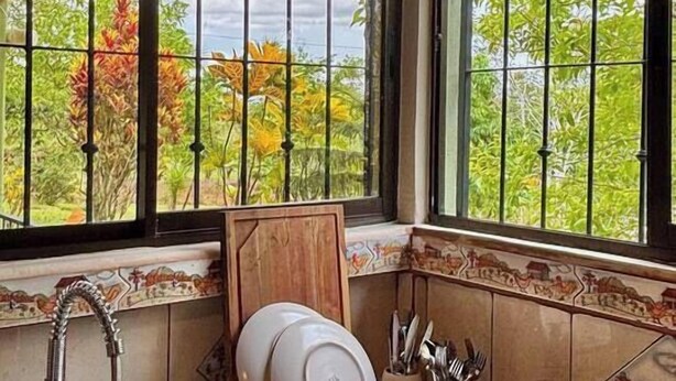 A kitchen with a sink, a dish rack, and a window with a view of greenery.