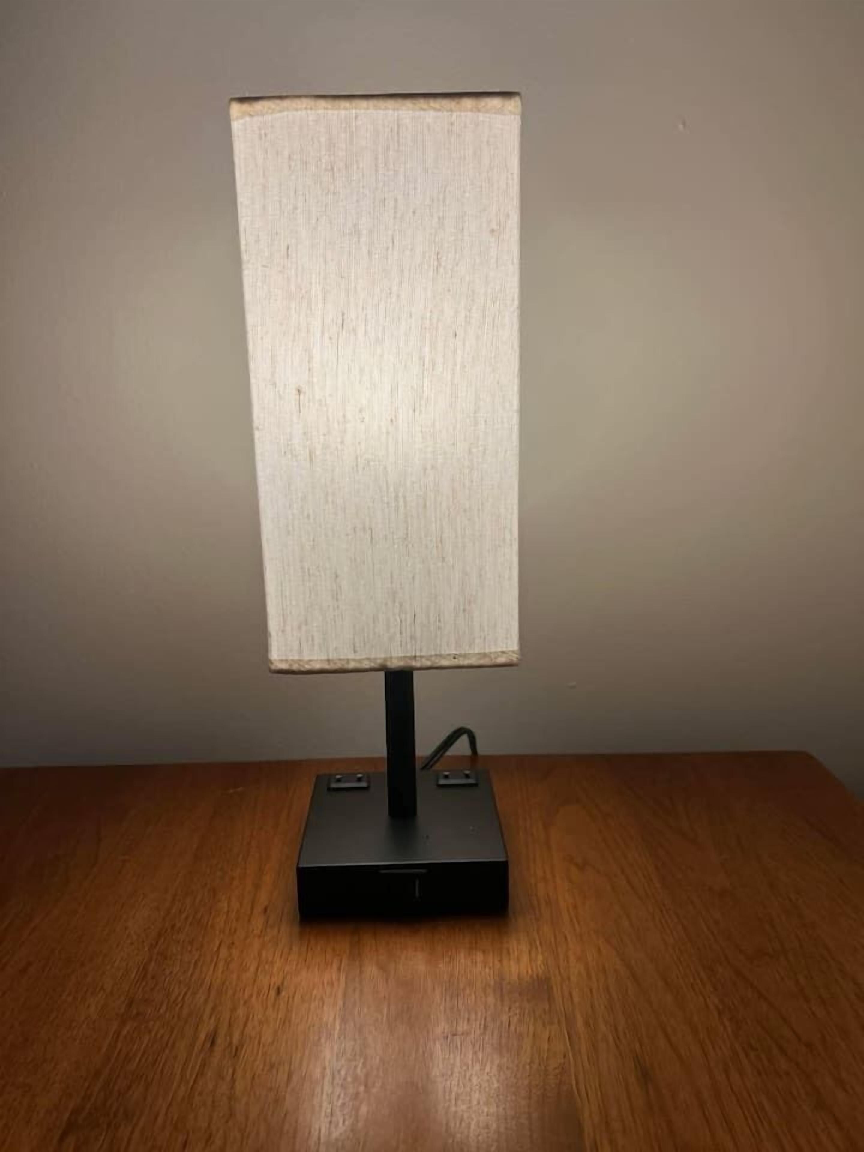 Een bureaulamp met een rechthoekige lampenkap op een houten tafel.