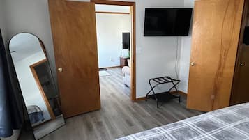 A bedroom with a bed, a wooden wardrobe, a mirror, a television mounted on the wall, and a door leading to another room.